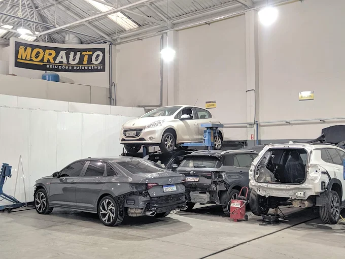 Área técnica da Morauto com carros em manutenção e cabine de pintura profissional ao fundo